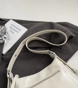 Detalle de correa ancha ajustable con ojales metálicos en bolso de piel color crema