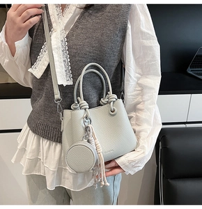 Close-up of light gray lychee grain bucket bag with coin purse and woven tassel detail