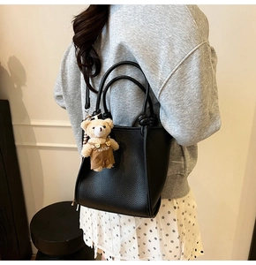 Detail of black lychee grain leather handbag with a cute brown bear plush charm attachment