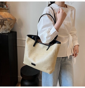 Detail view of woven straw tote bag featuring black contrast faux leather straps and knot accents