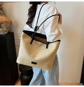 Detailed close-up of straw woven tote bag with black leather straps and brand logo