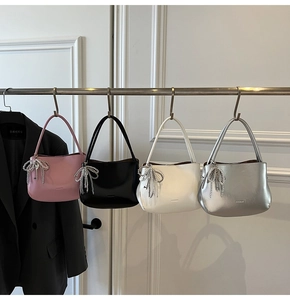 Detail of four glossy PU bucket bags with oversized rhinestone bow charms on a display