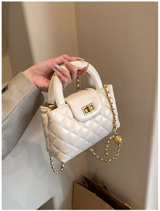 Close-up of beige quilted crossbody bag with gold ball chain and twist lock detail
