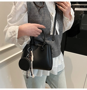 Black litchi grain leather bucket bag with mini purse charm shown on a model