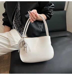 Detailansicht der weißen Beuteltasche mit CLEARUR-Logo und Perlenkette mit Herzanhänger