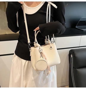 Detail of off-white bucket bag with woven knot handle and small round coin purse accessory