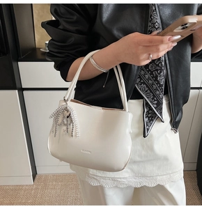 Details der weißen glänzenden Beuteltasche mit silberner Schlüsselkette und Logo-Prägung