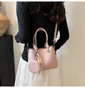 Pink bucket bag with litchi texture shown on model featuring woven tassel detail