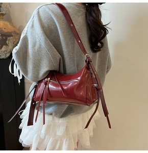 Detalle de bolso hobo granate brillante con cremalleras plateadas y correa ajustable