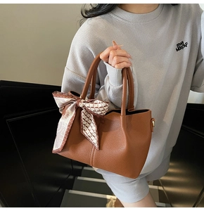 Détail d'un sac seau en cuir marron grainé avec foulard en soie géométrique au manche