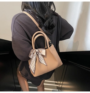 Détail du sac seau en cuir marron avec un foulard en soie géométrique sur la poignée ronde