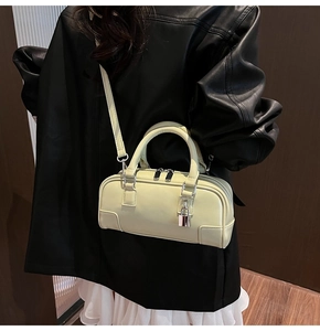 Close-up of a cream Boston bag with silver lock charm and adjustable shoulder strap