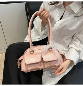 Detail of pink glossy Boston bag featuring front pockets and white lace bow decoration
