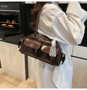 Detail of a brown patent leather Boston bag featuring front pockets and lace ribbon trim