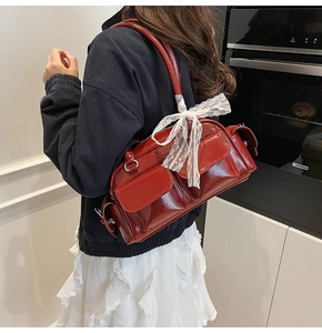 Detail of burgundy glossy leather shoulder bag with multi-pocket design and lace bow