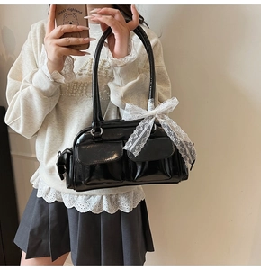 Detail of glossy black Boston bag with two front pockets and white lace bow decoration