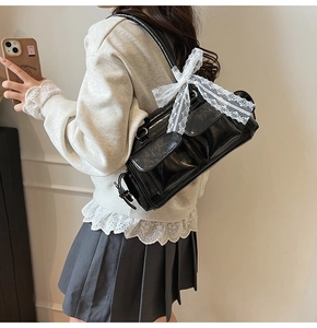 Detail view of glossy black Boston bag with a white lace bow and pocket details