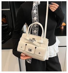 Close-up of cream handbag featuring triple front flap pockets with metal turn-lock closures