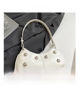 Détail d'un sac hobo en cuir beige avec des clous métalliques argentés sur un blazer gris