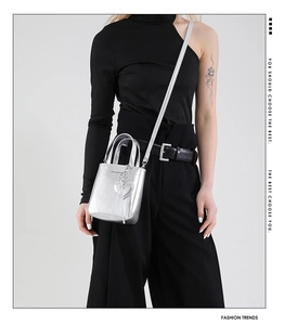 Detail of silver metallic mini bucket bag featuring a heart charm and crossbody strap