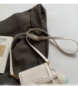 Detail of minimalist beige crossbody bag with gold buckle and fluffy charm on a blazer