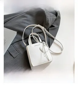 Detailed shot of white litchi pattern bucket bag with heart pendant on a grey blazer