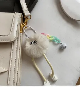 Detail of a white faux fur charm with big eyes and colorful chain on a stylish bag