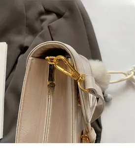 Detail of premium gold metal hooks and textured cream leather bag with pompom charm