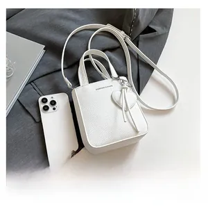 Close-up of white pebble-textured mini tote bag with heart charm and crossbody strap