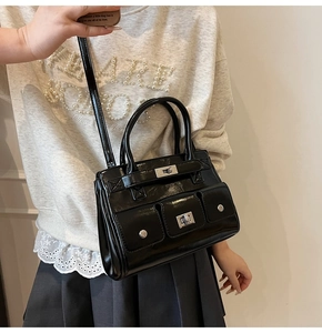 Close-up of black glossy crossbody bag with silver turn-lock pockets and metallic studs