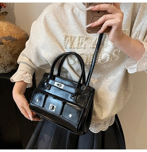Detail of black glossy patent leather tote bag with silver buckle and small front pockets
