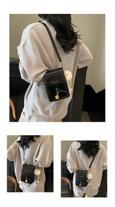 Detail of black leather shoulder bag with gold pendant and plush charm on a model
