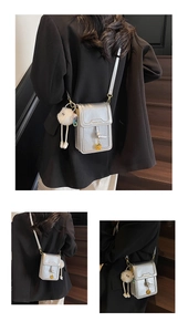 Detail of silver mini crossbody phone bag with fashion text and plush doll charm