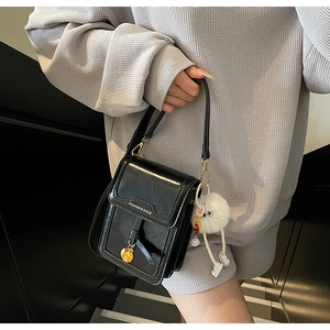 Detail of black glossy leather mobile phone bag with fashion text and furry ball charm