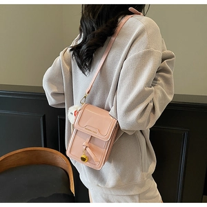 Detail of pink patent leather crossbody phone bag with plush ball and metal pendant