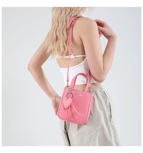 Pink mini leather tote bag with heart charm and crossbody strap shown on a model