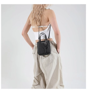 Detail of black lychee grain leather bucket bag featuring a heart charm and dual handles