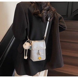 Detail of silver metallic crossbody phone bag with knot tassel and plush charm on black suit