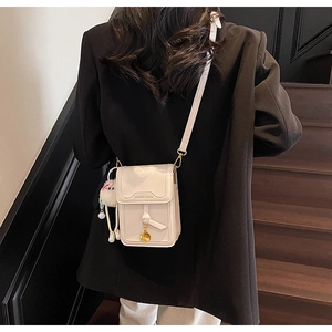 Detail view of a white mini leather crossbody bag with a cute white fur ball charm accessory