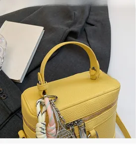Détail du sac boîte en cuir jaune avec charms tressés sur une veste grise