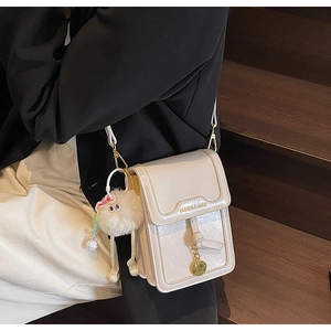 Detail of a beige leather shoulder bag with lychee texture and eye plush charm