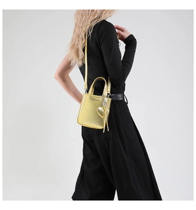 Detail of golden tote bag with heart charm, metallic fringe, and thin leather strap