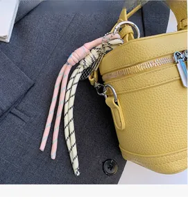 Détail d'un sac à main en cuir jaune avec breloque tressée rose et fermeture éclair argent
