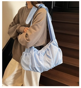 Close-up of light blue pleated cloud bag with adjustable knotted strap on shoulder