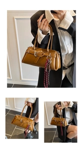 Brown leather Boston bag detail showing decorative belt with silver buckle and woven charm