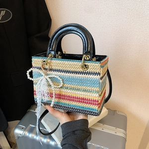 Sac à main tissé coloré avec poignées en cuir et breloque perle devant une valise
