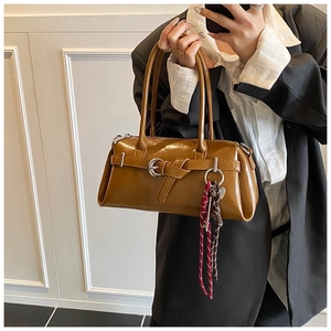 Detail of glossy brown leather handbag with silver buckle and braided charm pendant