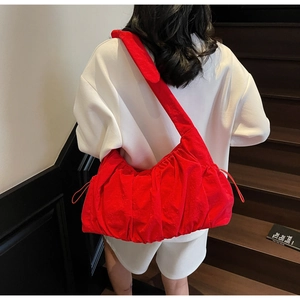 Large red nylon tote bag with pleated details shown on a model's shoulder in a lifestyle setting