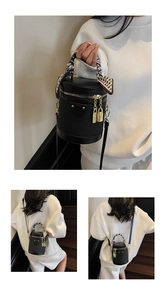 Close-up of black woven bucket bag featuring gold charm and silk scarf wrapped handle