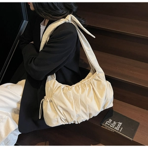 Detalle de un bolso nube plisado beige con textura de tela y correa ancha ajustable al hombro